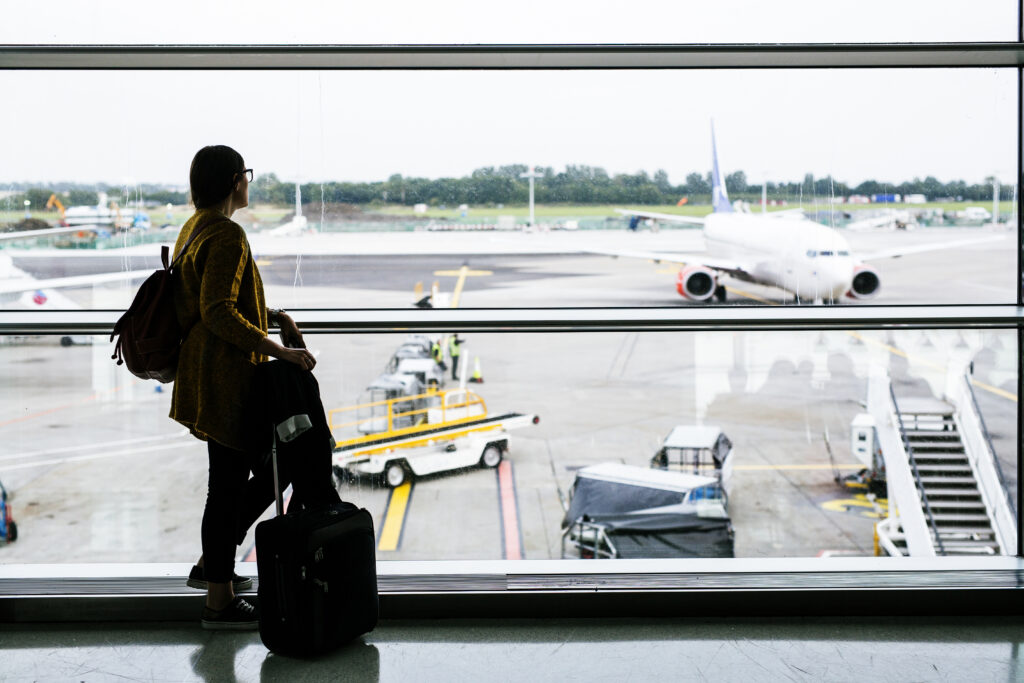Traveler standing at an airport terminal window watching an airplane before an international flight.
