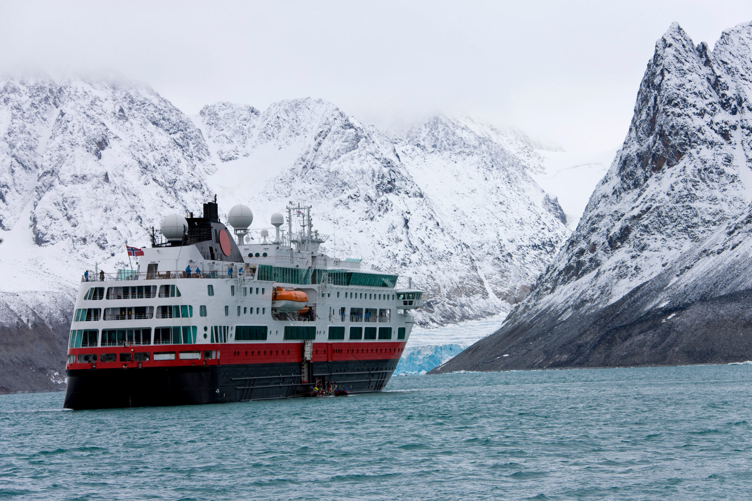 Expedition cruise ship navigating Antarctic waters surrounded by snow-covered mountains and glaciers during a polar voyage.
