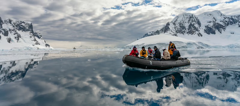 Travelers exploring Antarctica by Zodiac boat surrounded by glaciers, icebergs, and snow-covered mountains during a guided polar expedition.