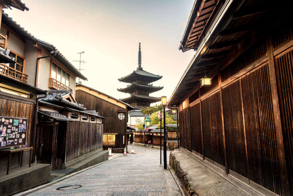 Traditional wooden buildings line a quiet cobblestone street leading toward Yasaka Pagoda in Kyoto, Japan, highlighting the city's historic architecture.